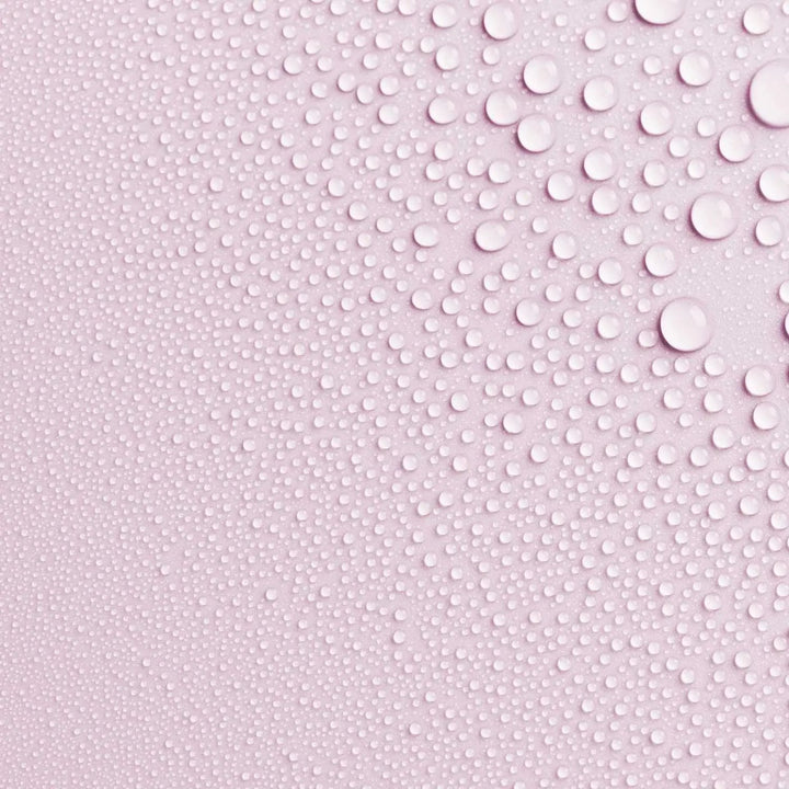 Close-up photo of AntiBeauty Fragile Soothing Toning Mist texture, with fine mist droplets on a pastel pink background.