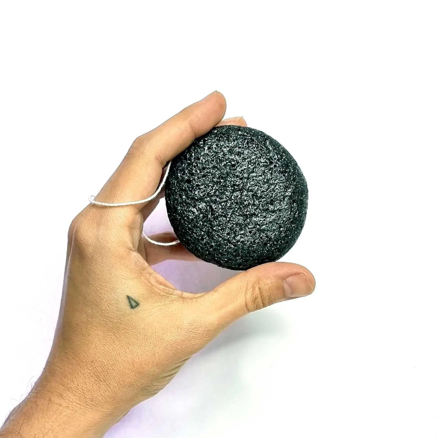 Hand holding a black AntiBeauty Konjac Sponge on a white background.