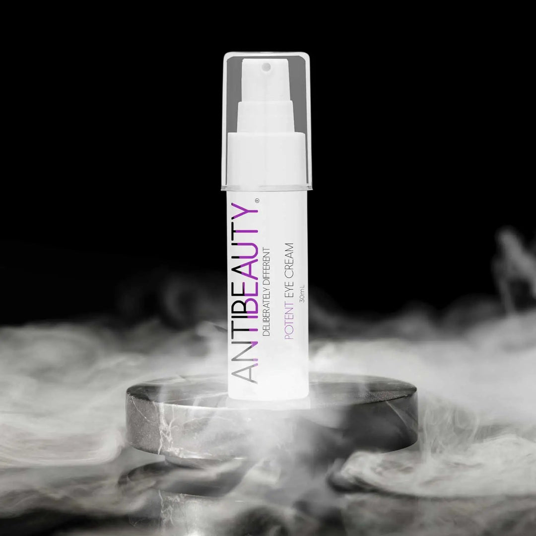 AntiBeauty Potent Eye Cream - a gentle eye cream for all skin types - on an black stone podium in front of a black background with white smoke.