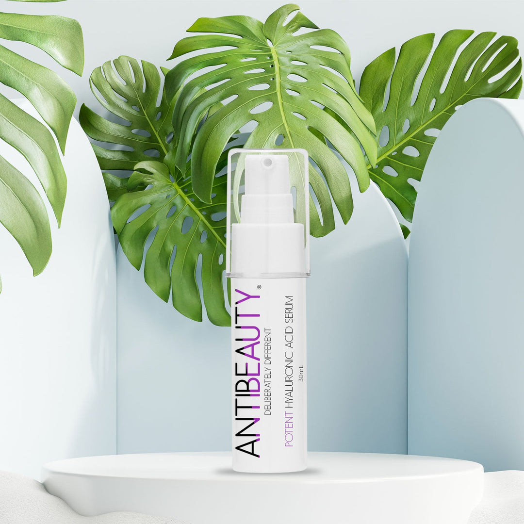 AntiBeauty Potent Hyaluronic Acid Serum - an ultra hydrating serum for dry skin, acne-prone, or ageing skin - on a white platform background with plants.