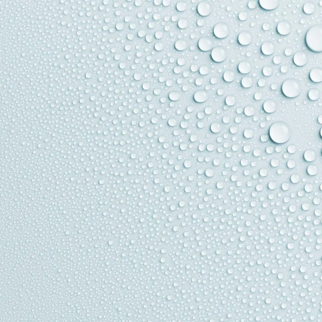Close-up photo of AntiBeauty Saturate Refreshing Toning Mist texture, with fine mist droplets on a pastel blue background.