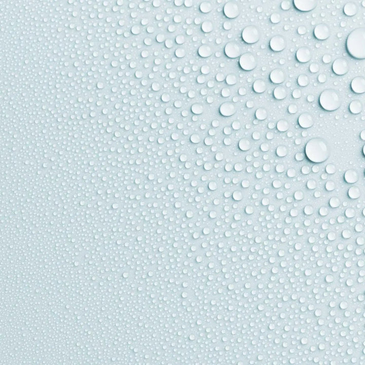 Close-up photo of AntiBeauty Saturate Refreshing Toning Mist texture, with fine mist droplets on a pastel blue background.